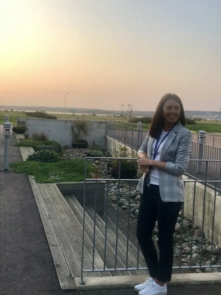 Hanna Ekman, HR Business Partner på Ringhals Kärnkraftverk, Vattenfall står utomhus med öppen landskapsvy bakom. Hanna har brunt hår och bär en vit kavaj och mörka byxor.