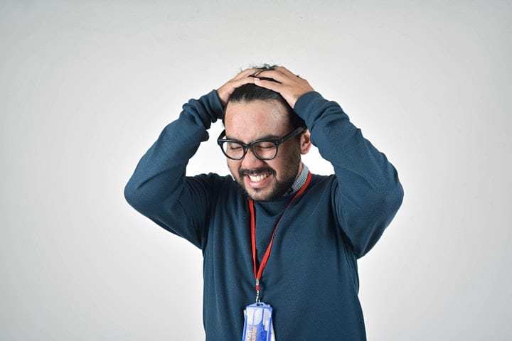 En person håller bekymrat händerna över sitt huvud med grå bakgrund