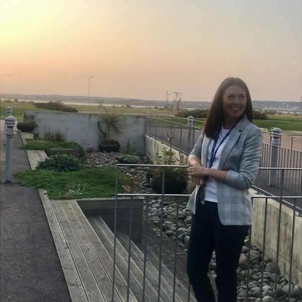 Hanna Ekman, HR Business Partner på Ringhals Kärnkraftverk, Vattenfall står utomhus med öppen landskapsvy bakom. Hanna har brunt hår och bär en vit kavaj och mörka byxor.